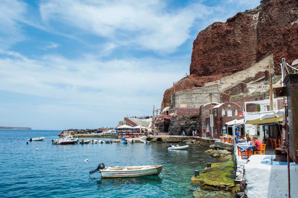 Small boats and waterfront tavernas at Ammoudi Bay beneath Oia's red cliffs