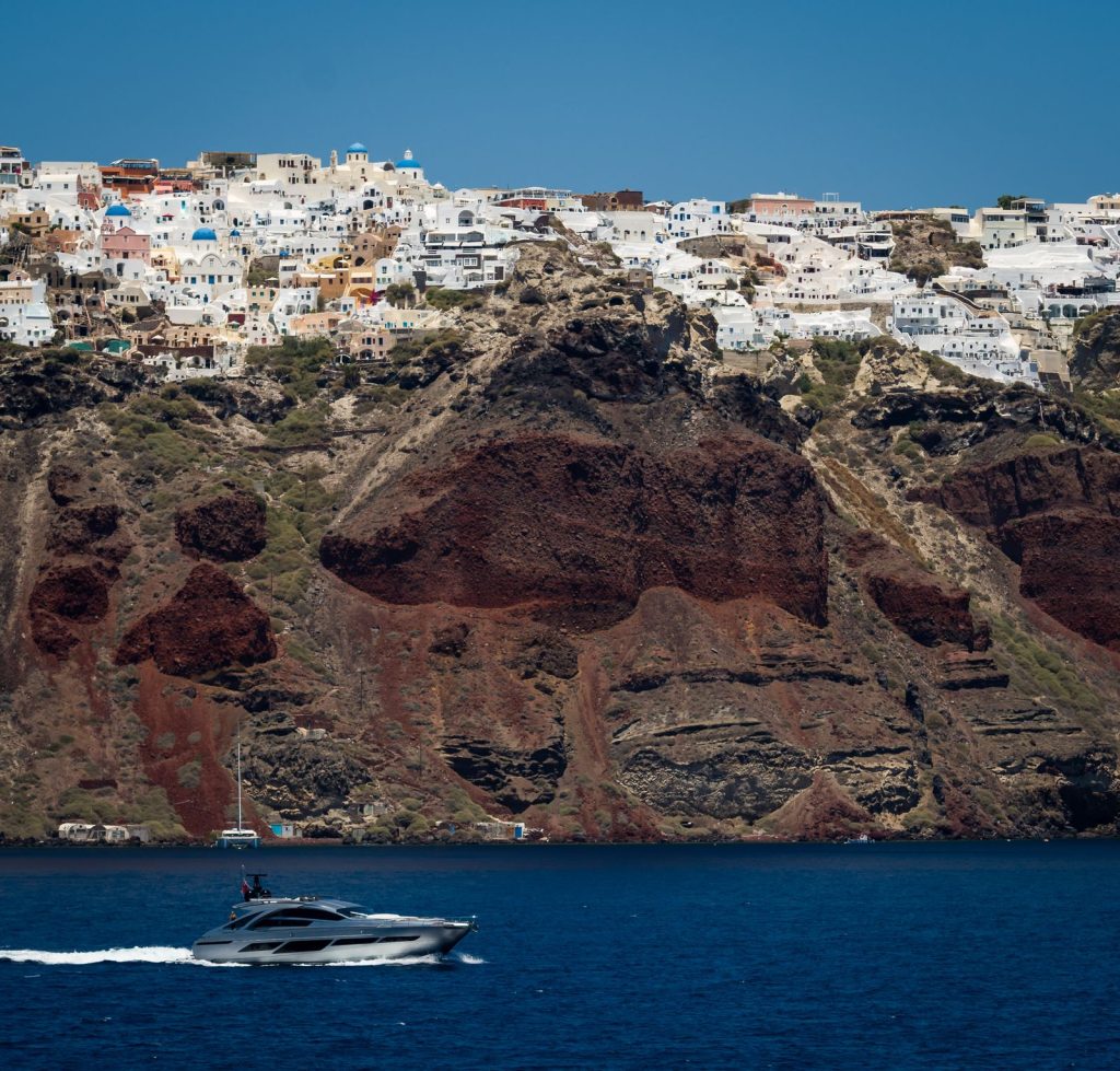 Boats crossing the Santorini caldera beneath the red cliffs below Oia